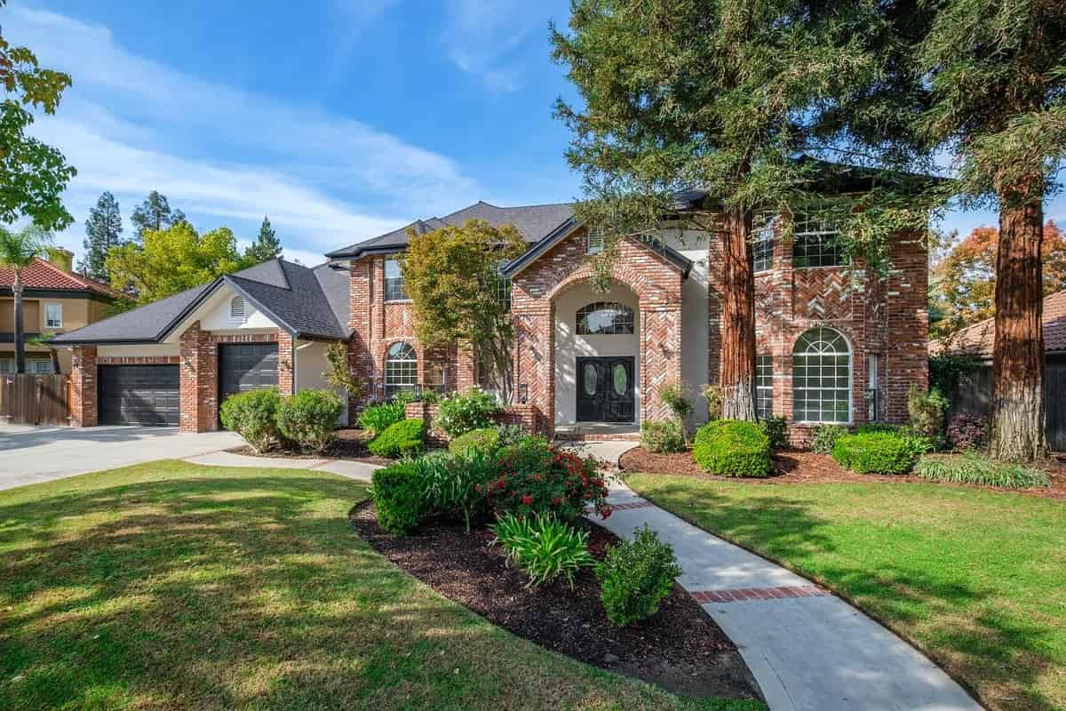 a brick home with a driveway and trees in the background