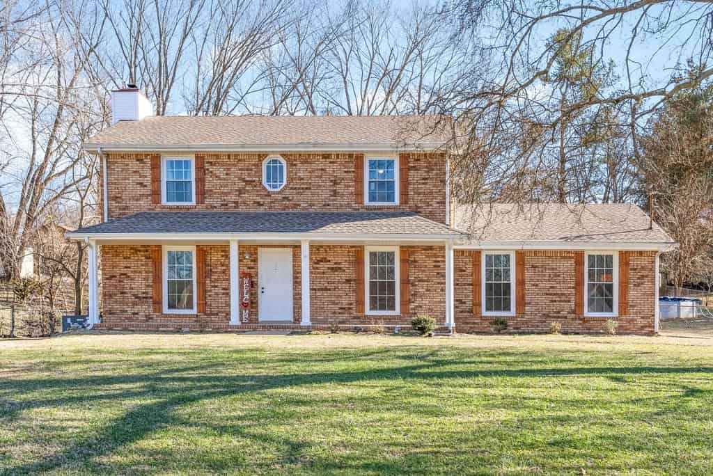 a brick house with a large yard and trees in the background