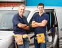 Two smiling male workers in tool belts standing next to a service van
